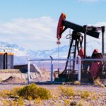 Oil pumpjack and tanks with a mountain backdrop under a blue sky